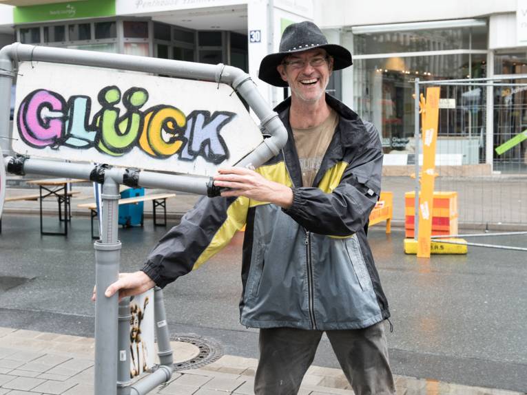 Ein fröhlicher Mann neben einem selbstgemachten Schild mit der Aufschrift "Glück"