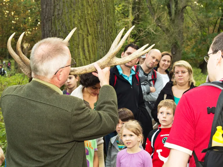 Ein Förster hält ein Geweih in den Händen und erklärt interessierten Besucherinnen und Besuchern, was es damit auf sich hat