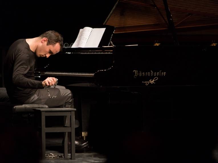 Igor Levit am Flügel, in der rechten Hand eine Eisenkette