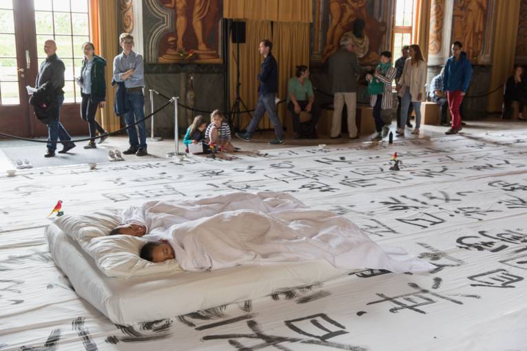 Szenenfoto von "We apologize to inform you" am 31. Mai in der Galerie Herrenhausen: Xiao Ke und Zi Han schlafend in einem weißen Bett, darum herum Publikum