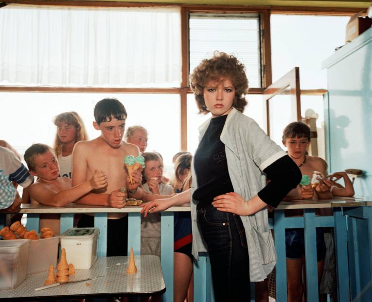 Junge Frau vor einem Tresen, dahinter Kinder mit Eistüten in der Hand.