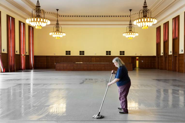 Frau wischt den Boden in einem leeren Saal.