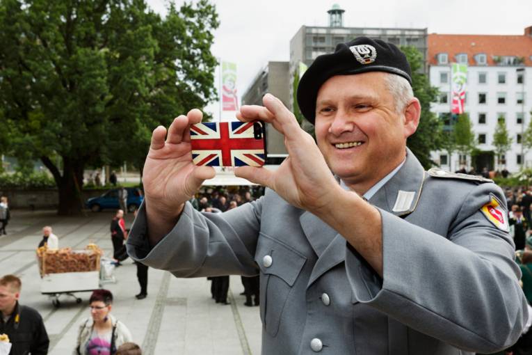 Ein Mann in Uniform fotografiert sich selbst mit einem Mobiltelefon, das die britsche Flagge als Muster trägt.