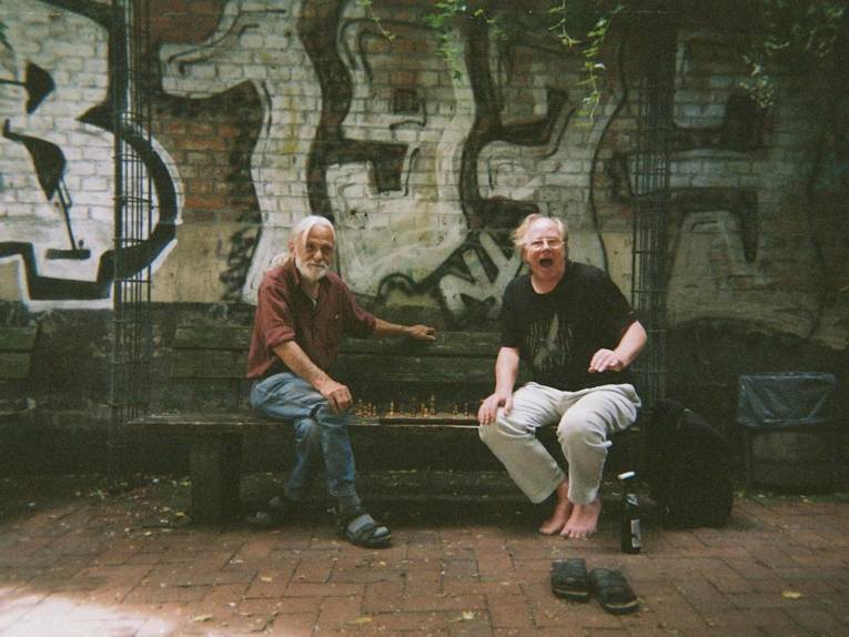 Fotografie, die zwei Männer auf einer Bank zeigt. 