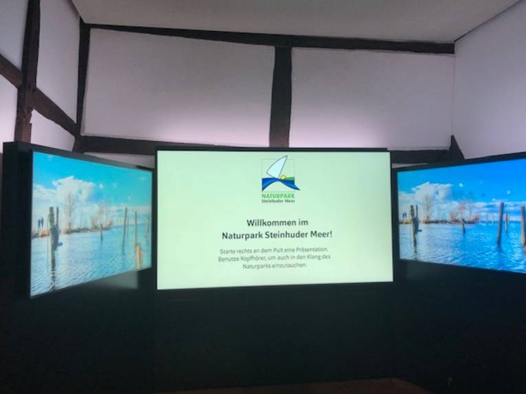 Ein großer Monitor zeigt den Text "Willkommen im Naturpark Steinhuder Meer!"