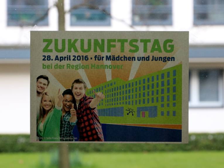 Ein Flyer klebt an der Fensterscheibe. 4 Jugendliche lächeln mit einer großen überschrift "Zukunftstag"