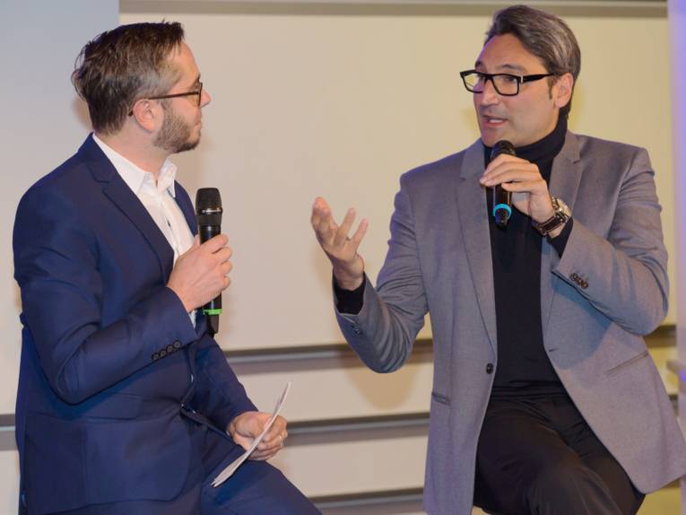 Zwei Männer sitzen sich gegenüber und sprechen in Mikrofone.