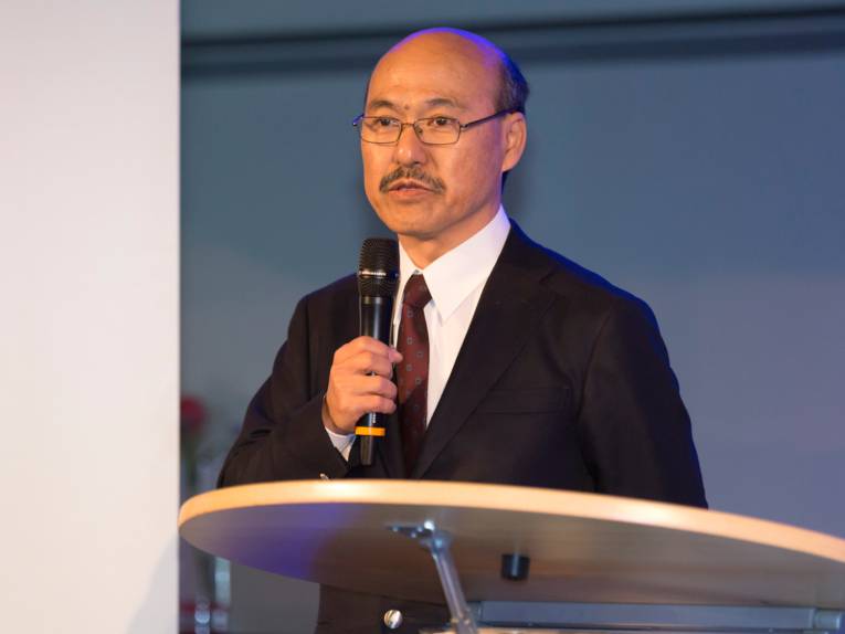 Ein Mann steht hinter einem Rednerpult und hält ein Mikrofon in der rechten Hand.