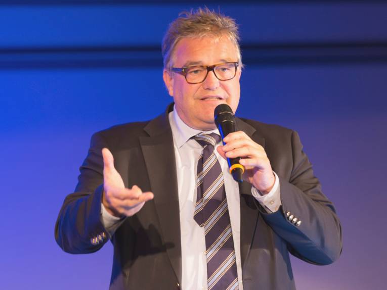 Ein Mann hält ein Mikrofon und spricht zum Publikum.