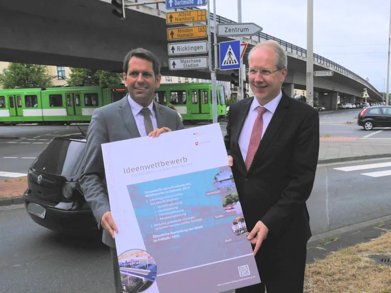 Zwei Männer in Anzügen halten ein Plakat hoch.