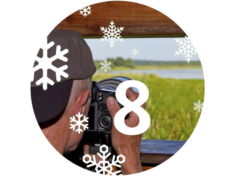 Ein Mann ist an einem Aussichtspunkt und schaut durch den Sucher seiner Kamera auf ein Feuchtgebiet.