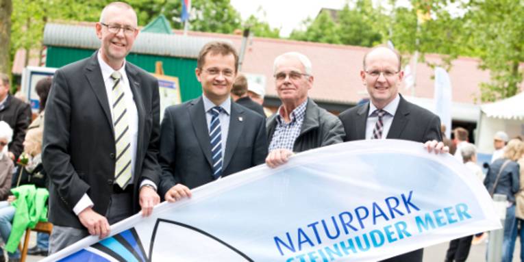Vier Männer stehen nebeneinander und halten dabei eine Strandflagge.