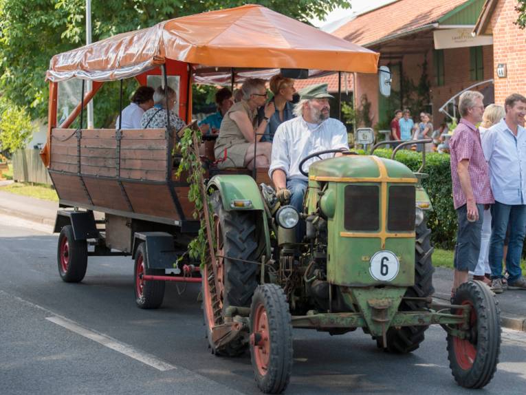 Ein Oldtimer-Trecker zieht einen Planwagen, darauf fahren Menschen mit.