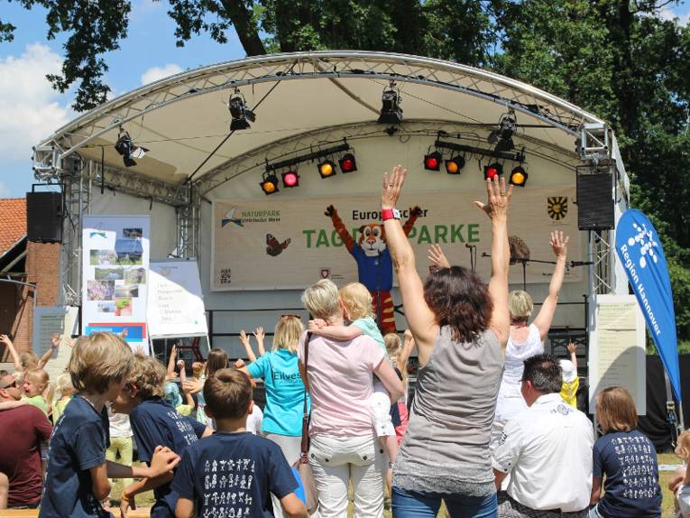 Menschen tanzen vor einer B&uuml;hne, darauf tanzt ein Maskottchen im Tigerkost&uuml;m.