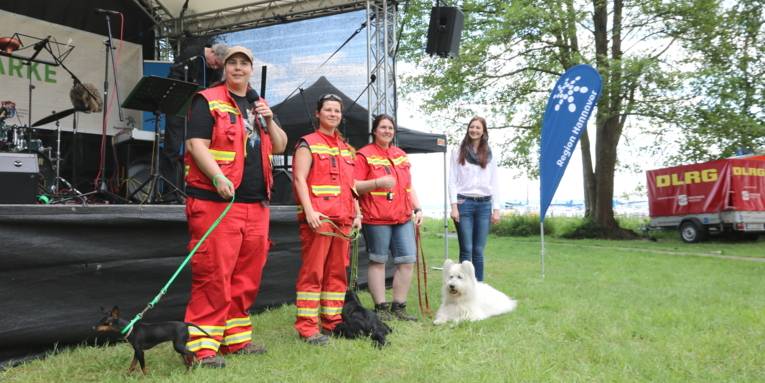 Vier Menschen und drei Hunde stehen vor einer Bühne.