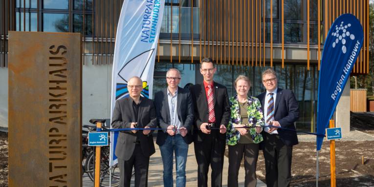 Vier Männer und eine Frau durchschneiden ein Band vor der Tür des Naturpark-Hauses am Steinhuder Meer.
