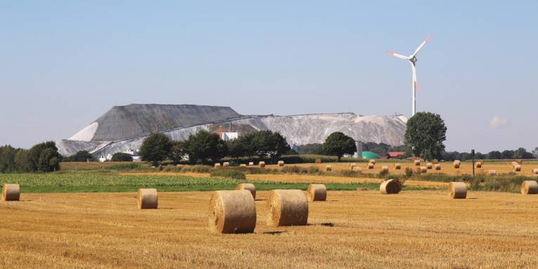Stoppelfeld mit Strohballen, dahiner sind ein Kaliberg und Windräder zu sehen.