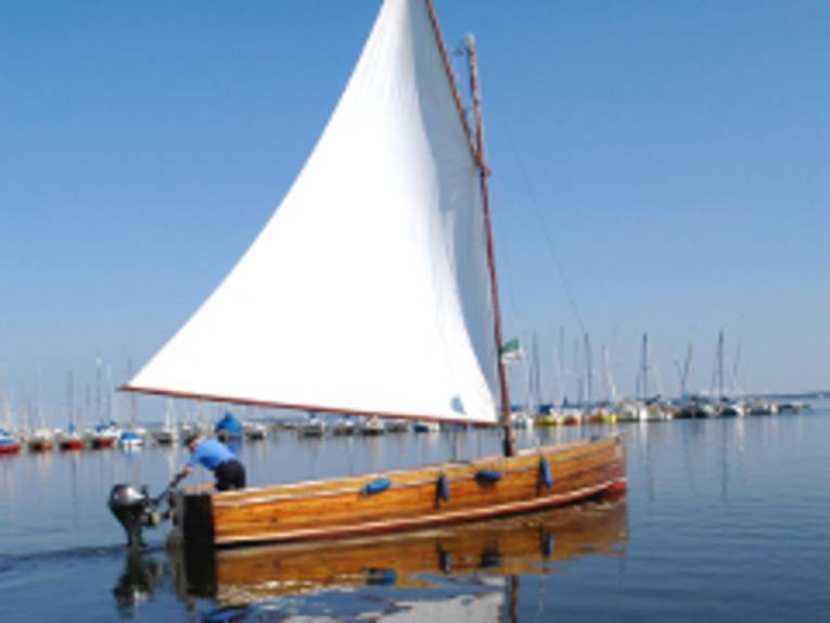 Ein Auswandererboot, eine offene Segeljolle, fährt als Ausflugsboot auf dem Steinhuder Meer.