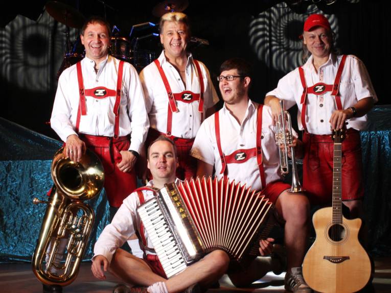 Fünf Männer in roten Lederhosen mit Instrumenten.