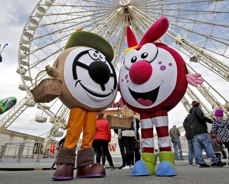 Zwei Maskottchen vor einem Riesenrad. 