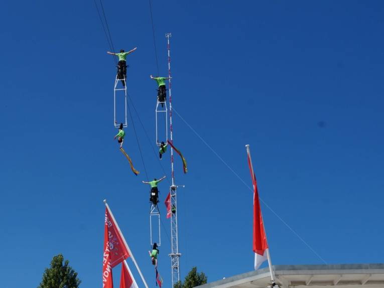 Artistinnen und Artisten auf Motorrädern über einem Platz. 