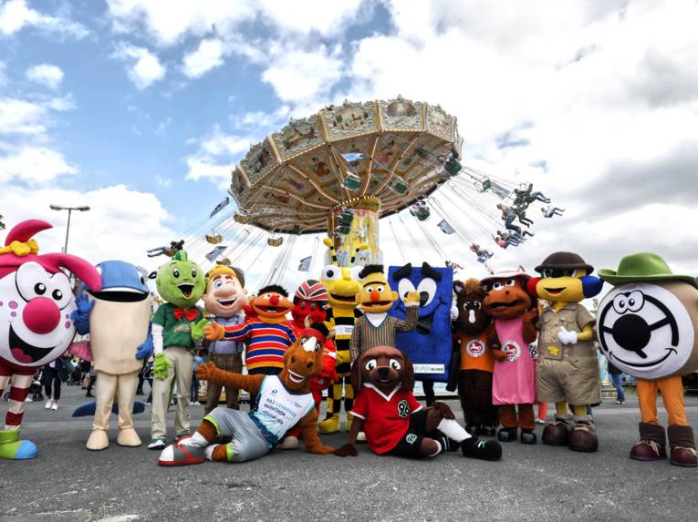 Maskottchen vor einem Kettenkarussell. 
