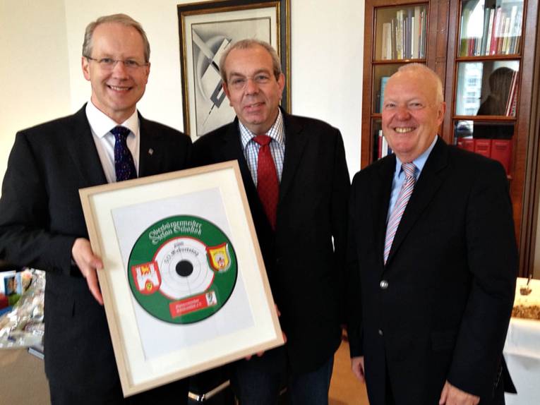 Drei lächelnde Männer mit einer Schützenscheibe. 