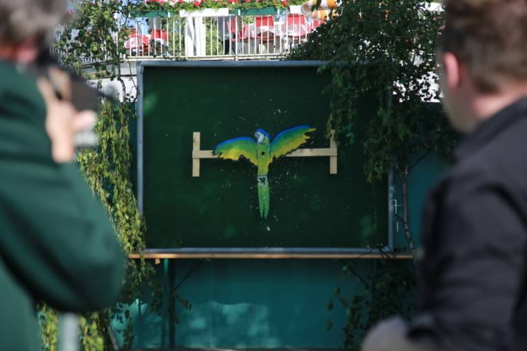 Menschen an einem Schießstand und in einer Festhalle. 