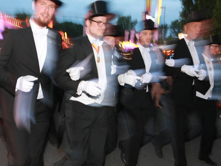 Männer in Cut und Zylinder auf einem Festplatz und in einem Zelt. 