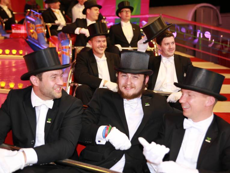 Männer in Cut und Zylinder auf einem Festplatz und in einem Zelt. 