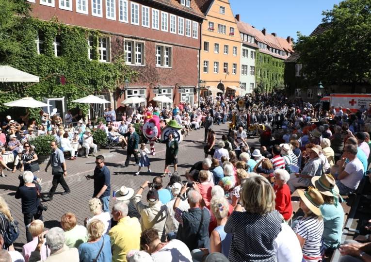 Menschen auf einem Platz, über den ein Umzug führt. 
