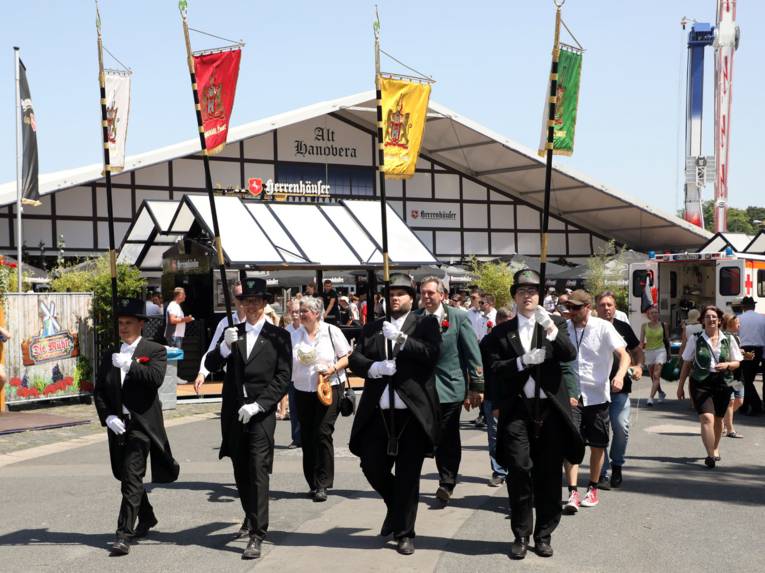 Menschen auf einem Festplatz. Um Vorfeld vier Männer mit Standarten. 