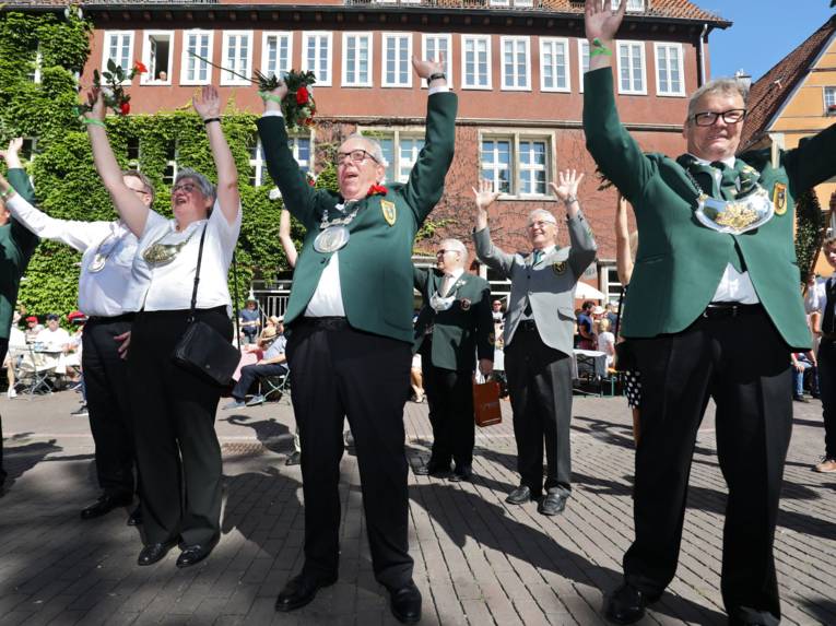 Uniformierte Menschen auf einem Platz. Sie reißen die Hände in die Höhe. 