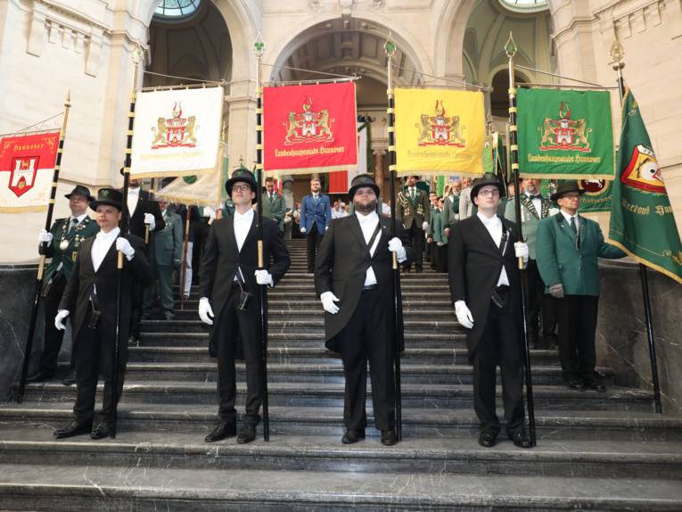 Vier Männer mit Standarten auf einer Treppe. 