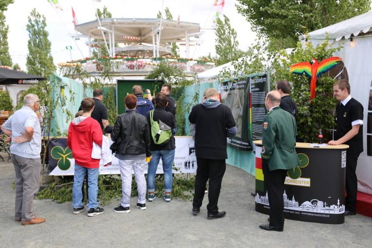 Menschen an einem Schießstand und in einer Festhalle. 