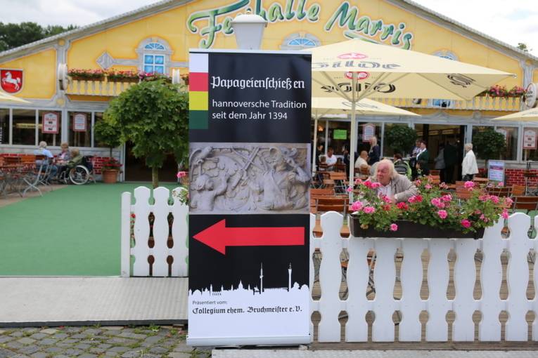 Menschen an einem Schießstand und in einer Festhalle. 