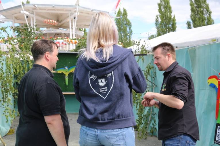 Menschen an einem Schießstand und in einer Festhalle. 