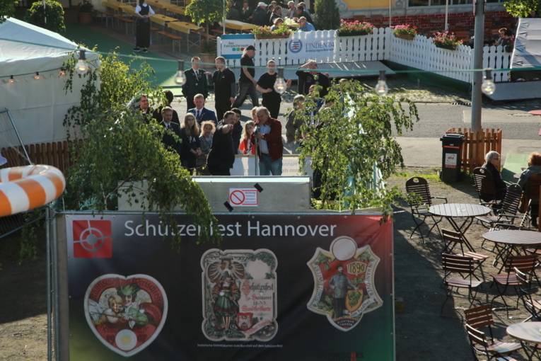 Menschen an einem Schießstand und in einer Festhalle. 