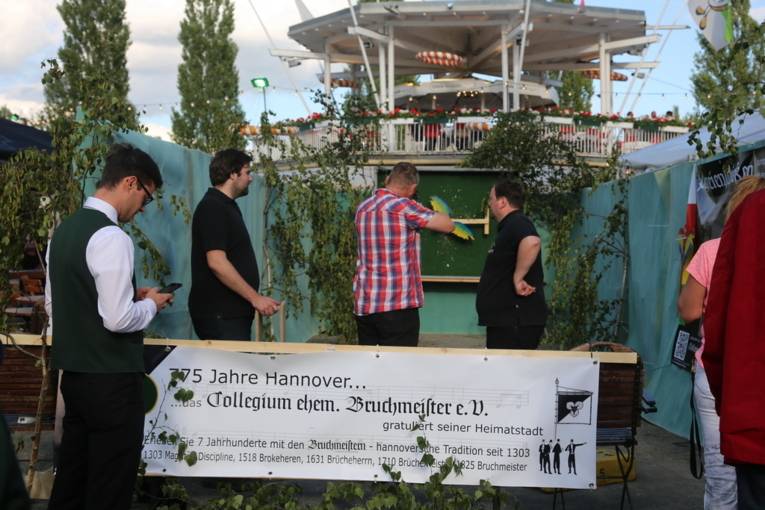 Menschen an einem Schießstand und in einer Festhalle. 