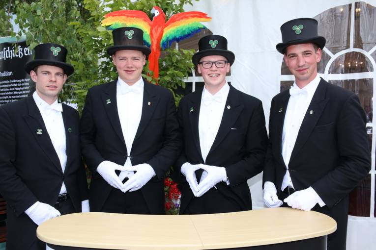 Menschen an einem Schießstand und in einer Festhalle. 