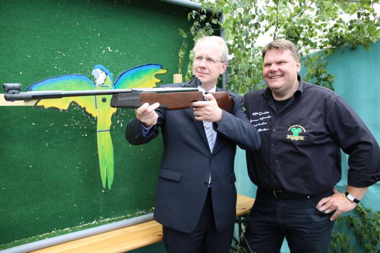 Menschen an einem Schießstand und in einer Festhalle. 