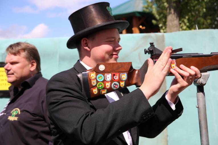 Menschen an einem Schießstand und in einer Festhalle. 