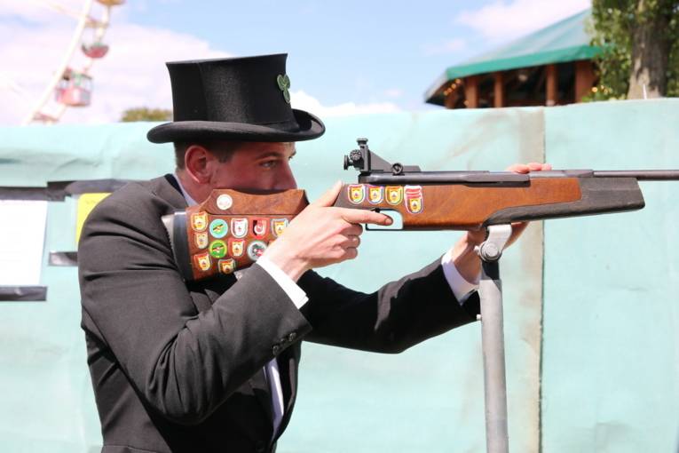 Menschen an einem Schießstand und in einer Festhalle. 