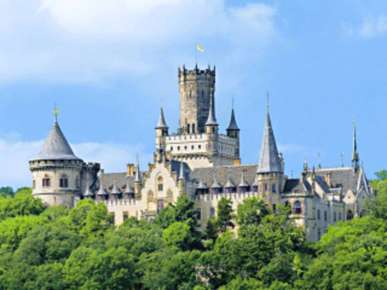 Das Schloss Marienburg aus einiger Entfernung: Türme ranken über grüne Bäume hinaus.