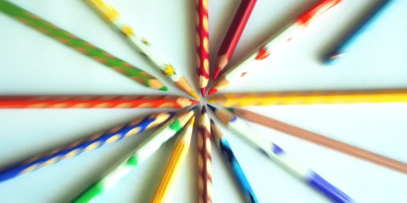 Buntstifte verschiedener Farben liegen auf einen wei&szlig;en Blatt Papier, durch den Reiss-Zoom-Effekt sind nur die Spitzen scharf.