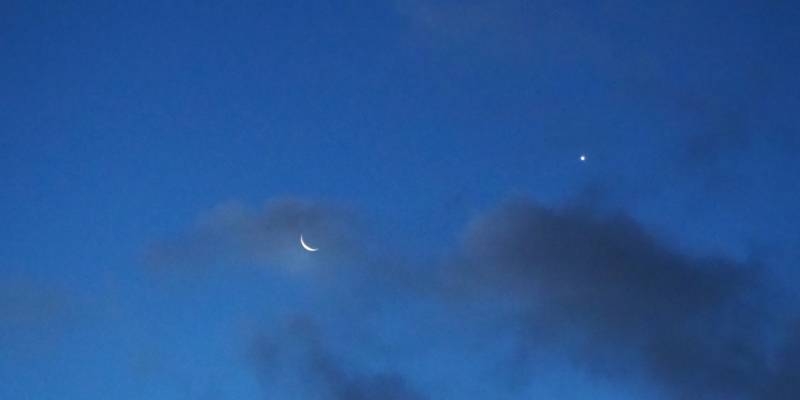 Abendhimmel mit Mond, einem Stern und dunklen Wolken.