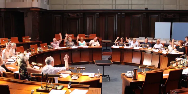 Etwa 20 Personen sitzen kreisf&ouml;rmig hinter Pulten im Hodlersaal im Neuen Rathaus. Die elf stimmberechtigten Mitglieder heben die Hand zur Abstimmung.