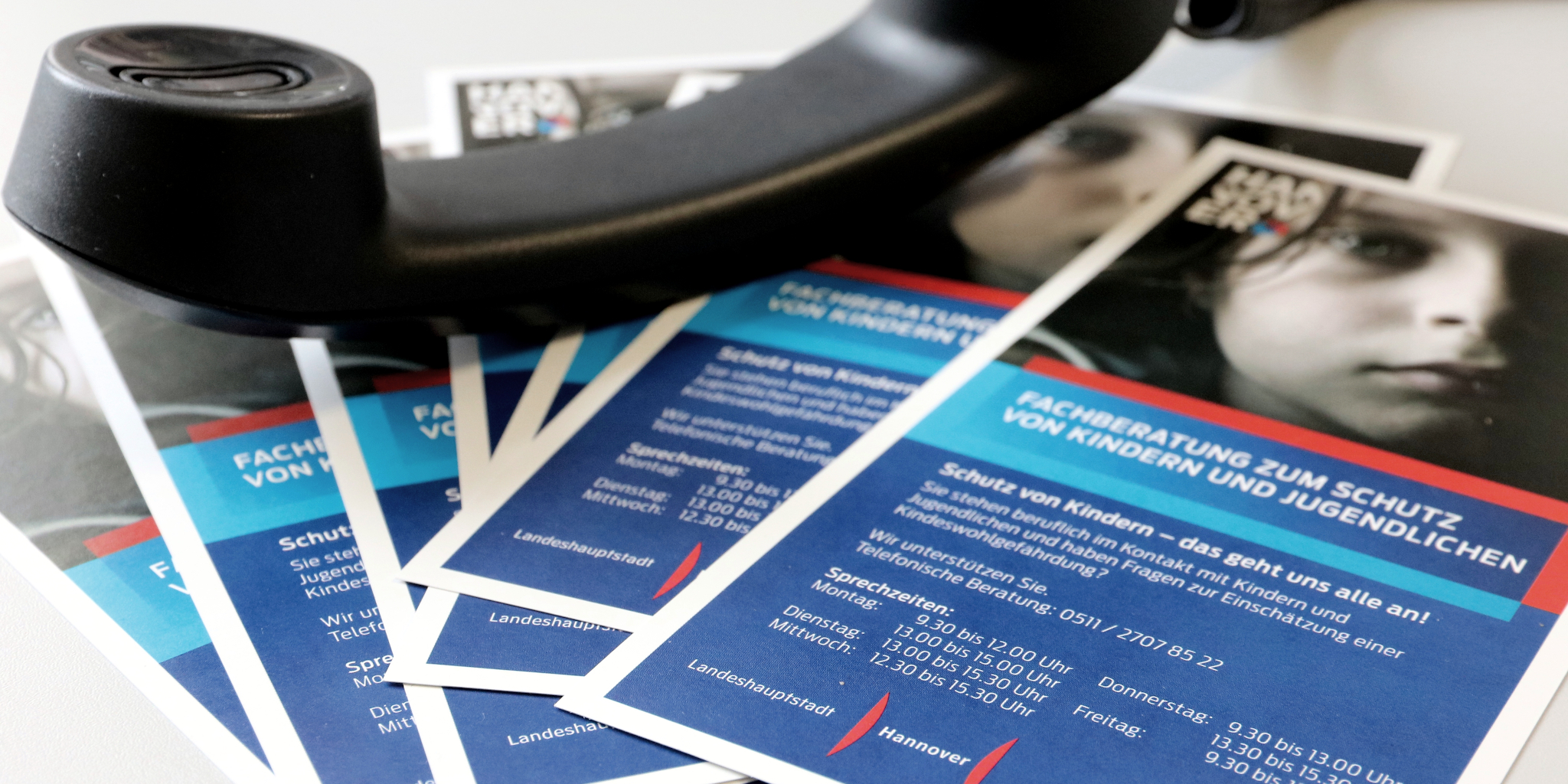 Mehrere Exemplare eines Flyers liegen aufgef&auml;chert auf einem Tisch. darauf liegt der H&ouml;rer eines Telefons.
